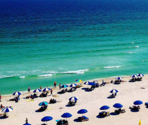 View of the beach in Pensacola Beach, FL with people and chairs with umbrellas for seating.