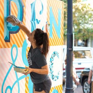 A woman painting on a wall spelling Pensacola